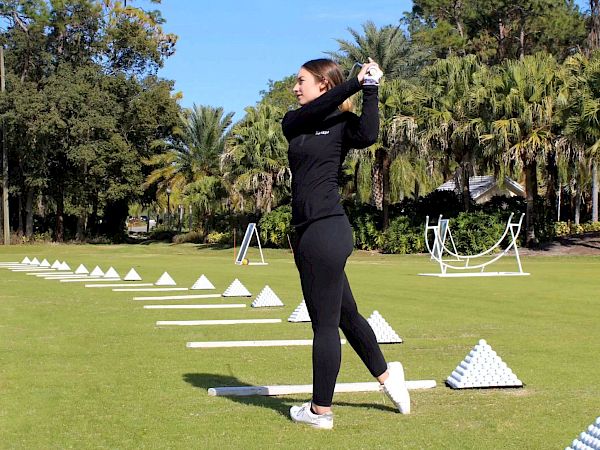 A person is practicing a golf swing at a driving range with pyramids of golf