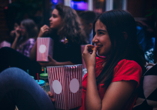 A person is smiling, holding popcorn, with others in the background.