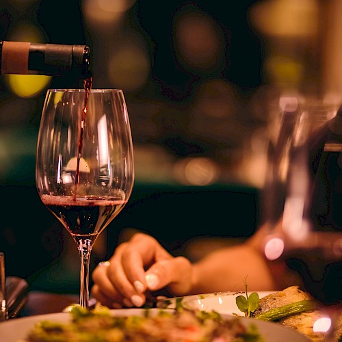 Red wine being poured into a glass at a cozy dinner setting.