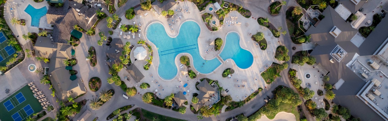 Aerial view of a resort with a kidney-shaped pool surrounded by buildings and greenery.