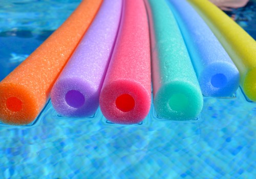 The image shows six colorful pool noodles floating on the surface of a swimming pool, half-submerged in the water.
