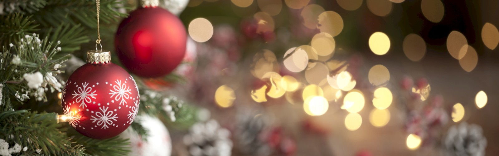 A Christmas tree with red and white ornaments and snowflakes is in focus, while festive lights and decorations blur in the background, creating a bokeh effect.