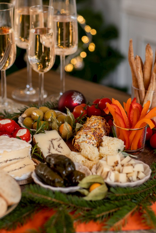 A festive spread with cheeses, fruits, bread, breadsticks, cutlery, and glasses of champagne on a decorated table.