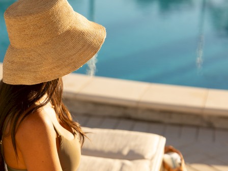 A woman wearing a large straw hat relaxing by a poolside on a sunny day.
