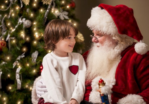 A child sits on Santa's lap beside a decorated Christmas tree, smiling and holding a toy in a festive setting.