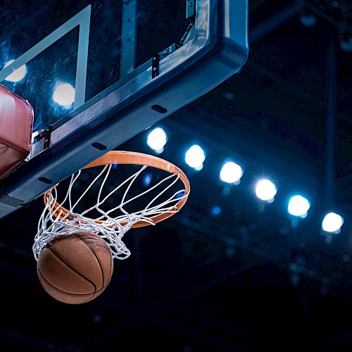 A basketball going through a hoop under stadium lights, viewed from below the basket.