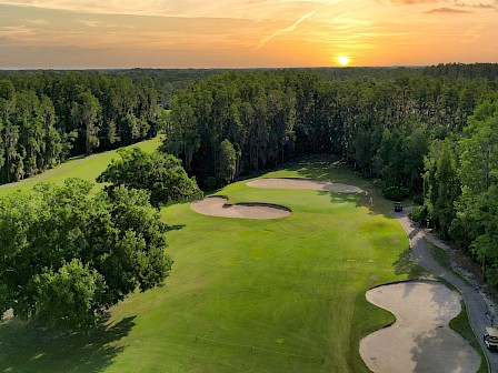 A scenic golf course with sand traps, surrounded by trees, under a sunset sky.