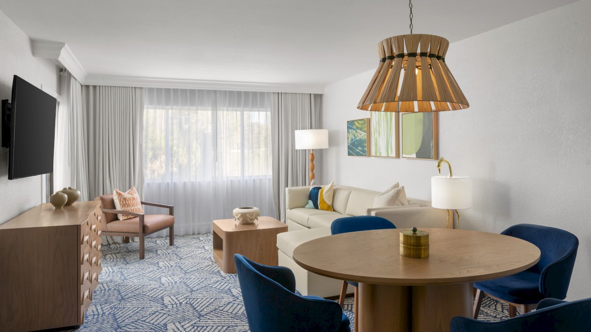 The image shows a modern living room with a sofa, chairs, TV, wooden furniture, and a stylish light fixture.