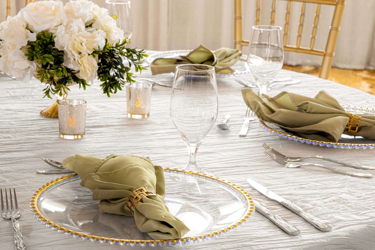 Elegant table setting with white and gold decor, green napkins, and a floral centerpiece.