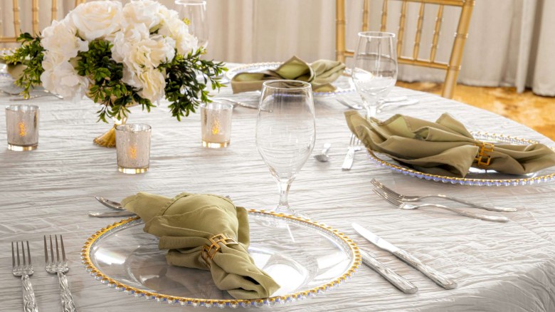 Elegant table setting with white and gold decor, green napkins, and a floral centerpiece.