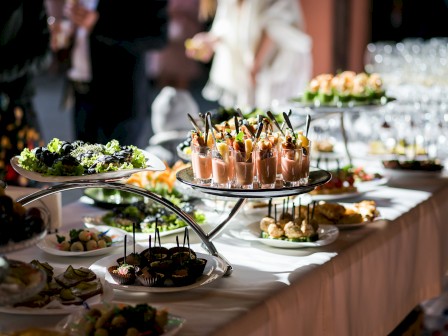 The image shows a buffet table with various appetizers, salads, and glasses, likely set up for an event or celebration.