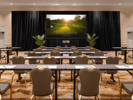 A conference room setup with rows of tables and chairs facing a large screen displaying 