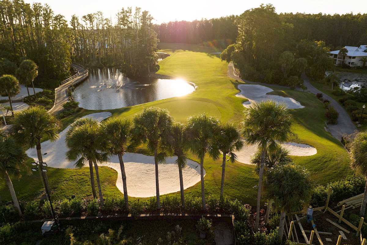 A scenic view of a golf course at sunset, featuring sand traps, water hazards, palm trees, and lush green fairways.