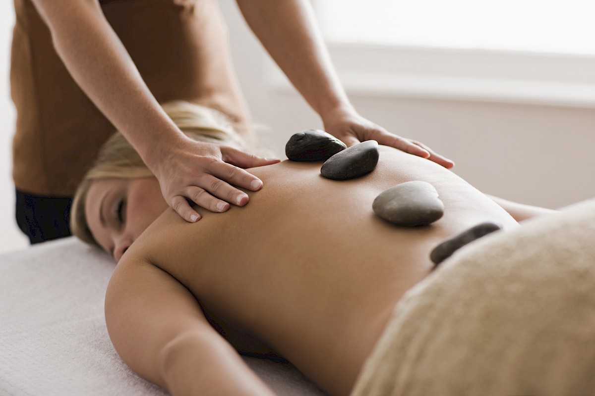 A person receiving a hot stone massage with smooth stones placed on their back and someone massaging their shoulders.