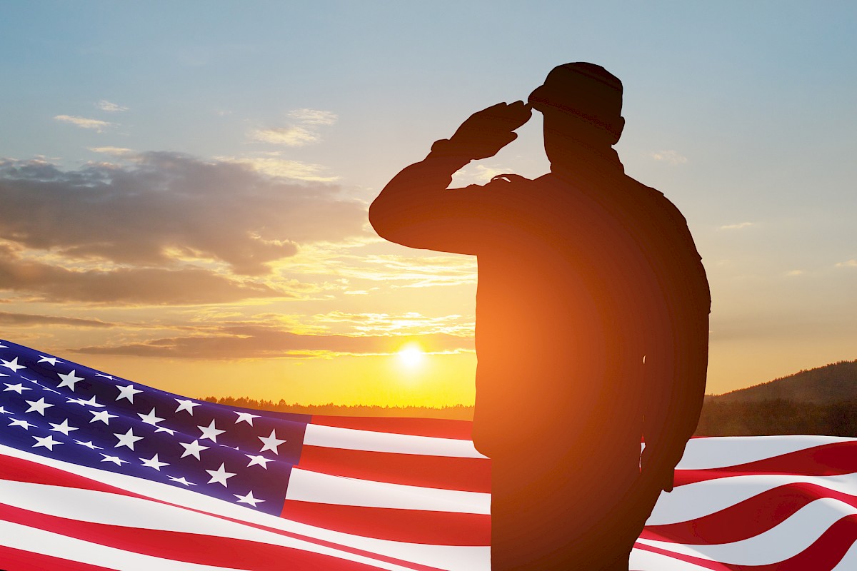 Silhouette of a person saluting at sunset with the U.S. flag in the foreground.