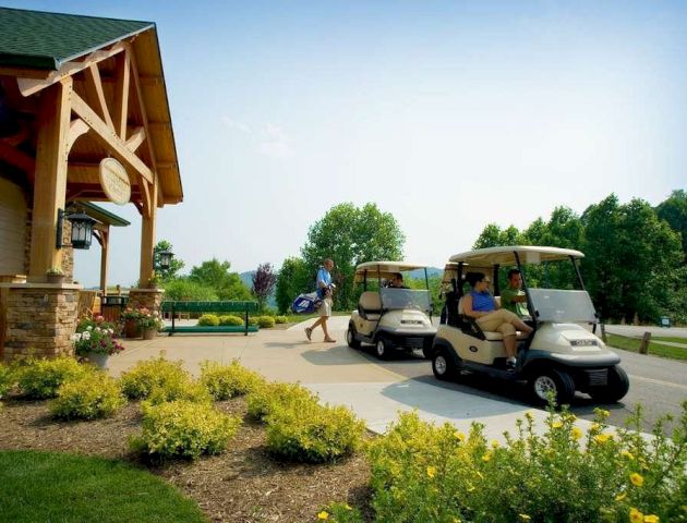 People are preparing for a golf outing outside a clubhouse, with some driving golf carts and one person carrying a golf bag.