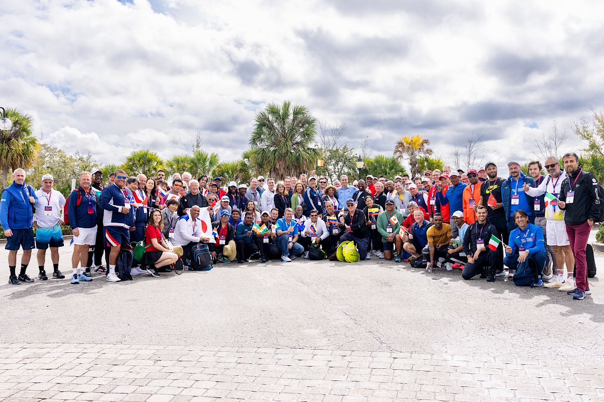 The image shows a large group of people outdoors, posing together for a group photo under a partly cloudy sky, ending the sentence.