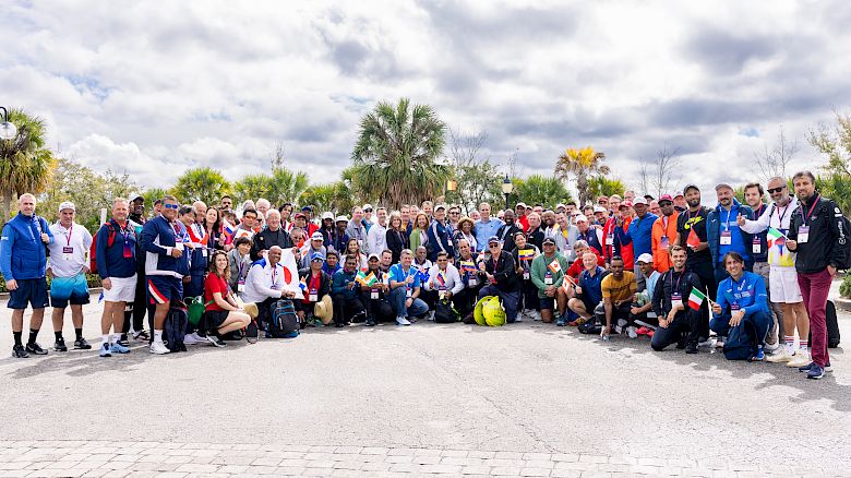 The image shows a large group of people outdoors, posing together for a group photo under a partly cloudy sky, ending the sentence.