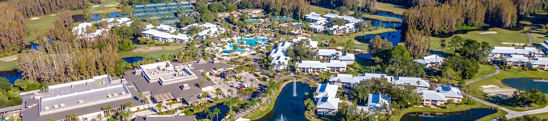 This image shows an aerial view of a resort area with buildings, a large pool, and surrounding greenery and water features.