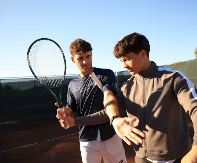 Two men aiming pistols in a scouting or action scene, wearing jackets, outdoors near a fence and vehicles, focused and alert.